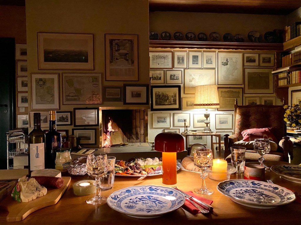 Altes Geschirr und moderne Lampe vor Kamin: Flackerndes Feuer sorgt für eine gemütliche Atmosphäre.